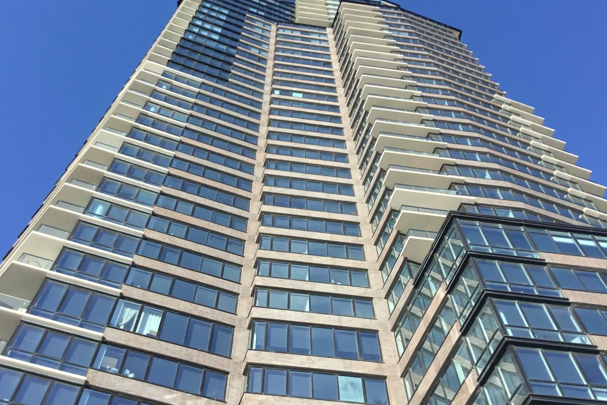 Upward view of The Greenpoint tower's glass and brick facade against a blue sky