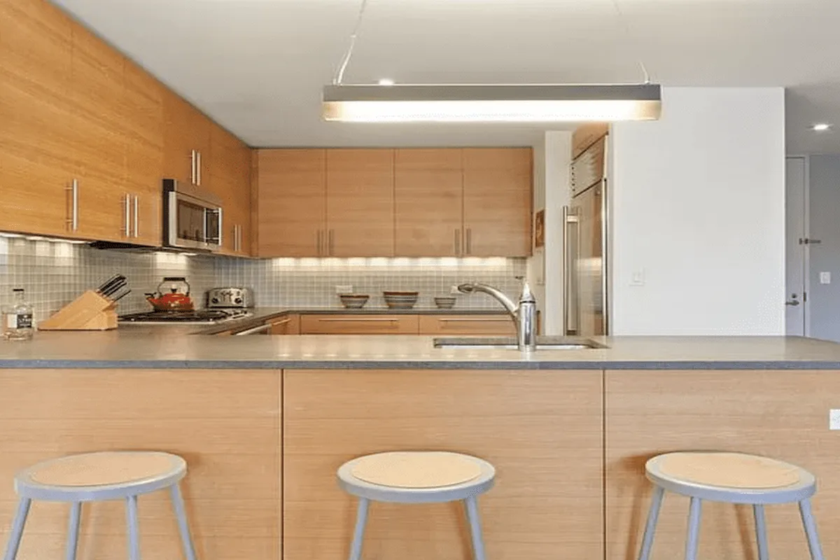 Open chef's kitchen with wood cabinetry, stainless appliances, and a peninsula island with bar stools