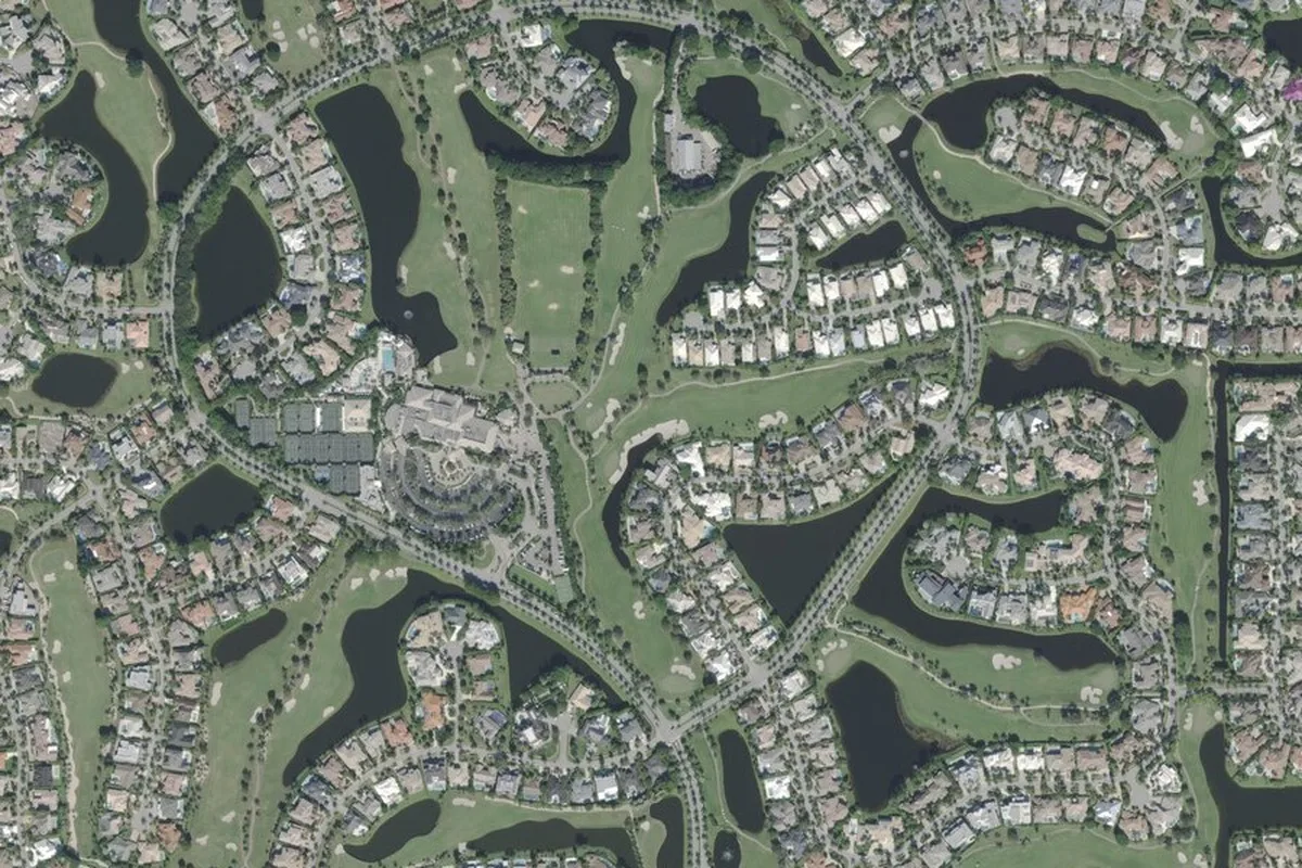 Closer aerial view of the St. Andrews clubhouse, tennis courts, and pool at the center of the community, ringed by fairways, lakes, and cul-de-sacs of estate homes