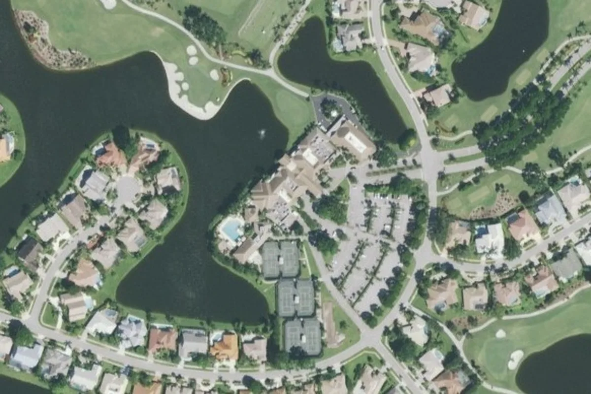 Aerial view of the Stonebridge clubhouse with its pool, tennis courts, and parking lot beside a golf course lake