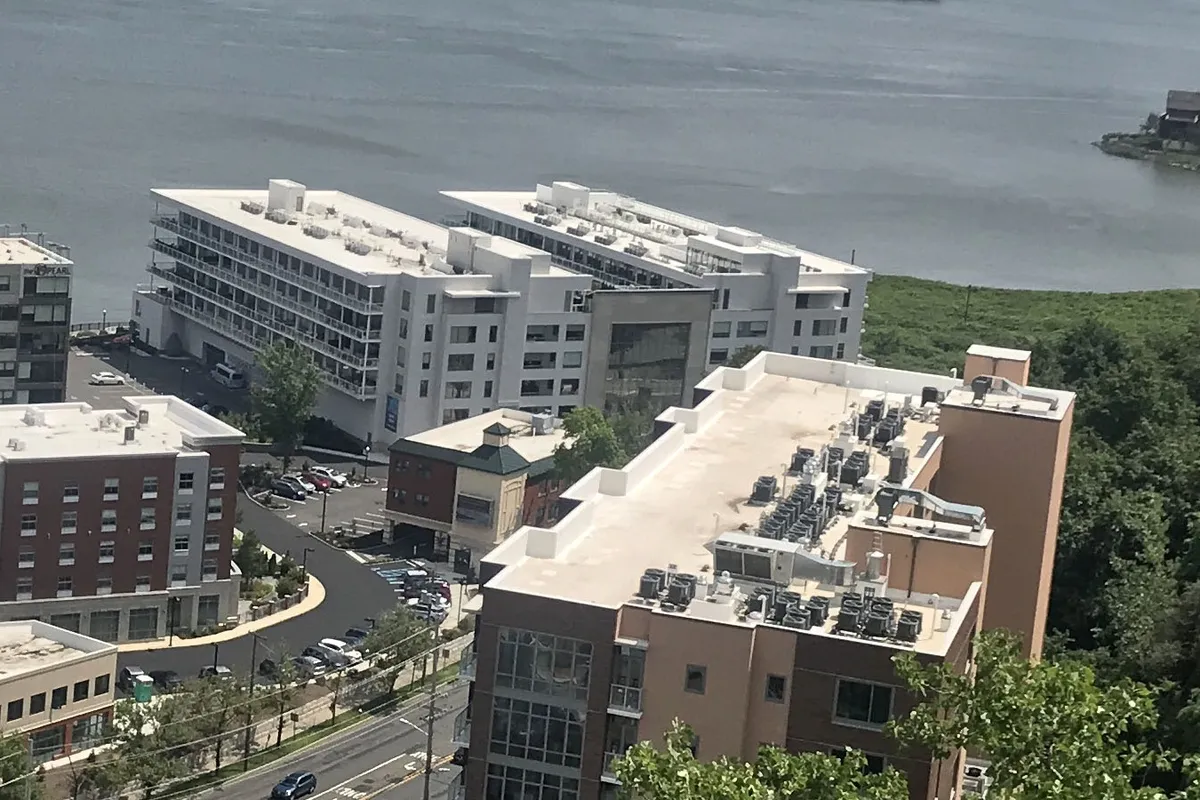 The Glass House seen from the Palisades, two white wings ringed with glass-railed terraces on the Hudson River shore beside The Pearl